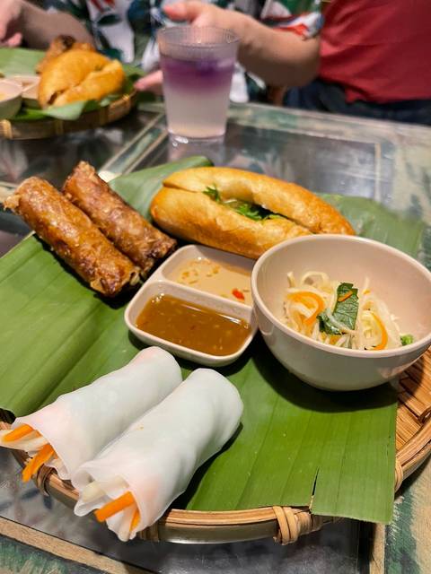 Vietnamese meal plate with spring rolls, baguette sandwich, dipping sauces and fresh salad on banana leaf