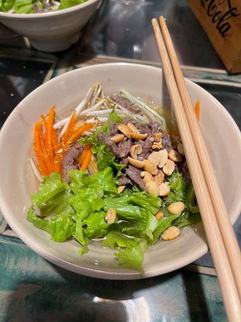 Bowl of Vietnamese noodle salad topped with beef, lettuce, peanuts and vegetables