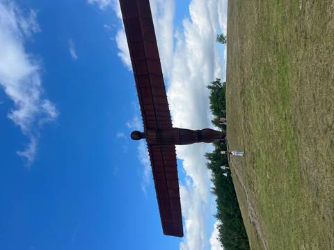 The monumental Angel of the North steel sculpture spreads its wings over grassy hillside.