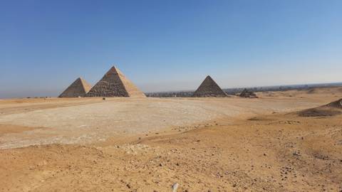 Wide desert scene featuring the iconic Pyramids of Giza under a clear blue sky.