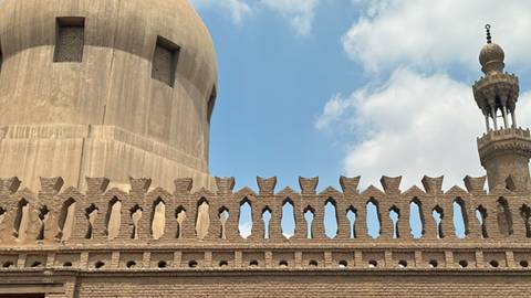 Close view of an old stone mosque wall with decorative crenellations and domed minaret.