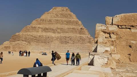 Visitors walk near the Step Pyramid of Saqqara under a cloudless sky.