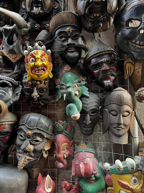 Colorful assortment of traditional Nepali wooden masks displayed on a market wall.