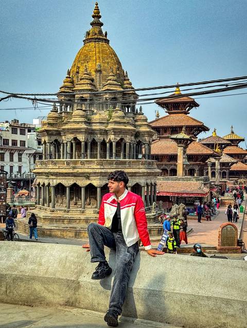 Traveler sitting on a ledge overlooking intricately carved temples in Kathmandu's Durbar Square on a hazy day.