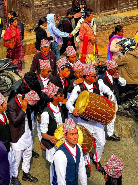 Traditional Nepali musicians in festive attire playing large drums during a street celebration.