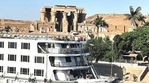 White Nile cruise boat docked with Kom Ombo Temple ruins visible on the opposite bank.