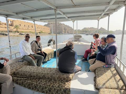 Travelers sit on cushioned benches of small motorboat approaching Philae Temple on Nile.