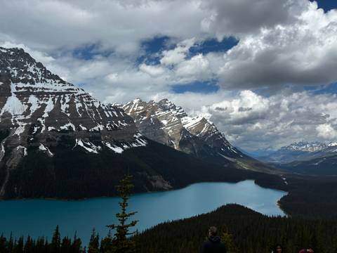 Turquoise Peyto Lake winding beneath rugged snow-dusted mountains under dramatic clouds.