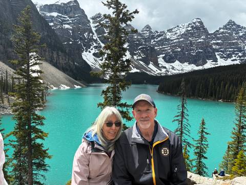 Smiling couple poses before Moraine Lake’s bright turquoise water and towering peaks.