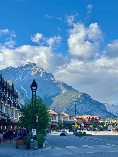 Sunlit Rocky Mountain peak with lingering snow rising behind alpine-style buildings and a small steepled tower.