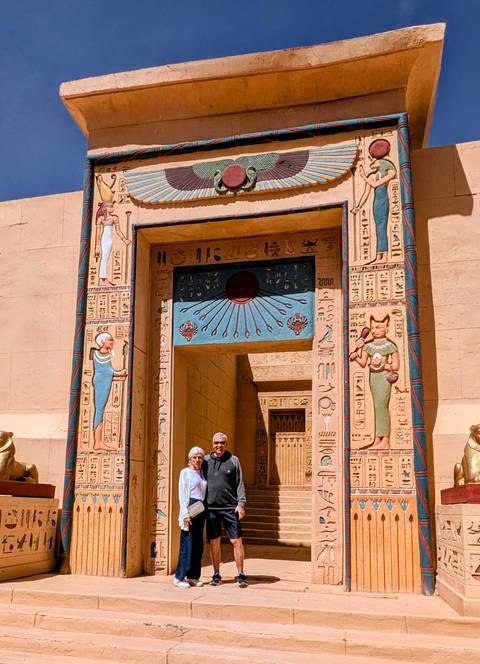 Older couple standing in front of an Egyptian-style film set gate covered with colourful hieroglyphs
