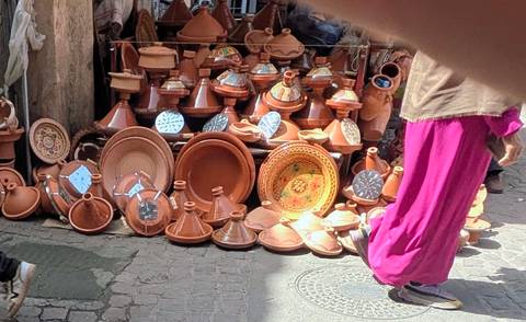 Street stall filled with terracotta tagine pots; partial hand and blurred finger in frame