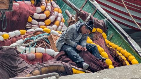 Fisherman mending colourful nets piled on a traditional wooden boat in a Moroccan port