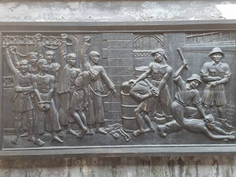 Detailed stone relief depicting chained prisoners and guards in a historical scene inside a museum.