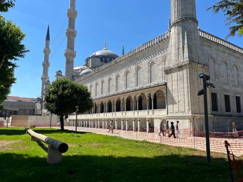 Exterior of the Blue Mosque with minarets under a clear blue sky and visitors walking in front.