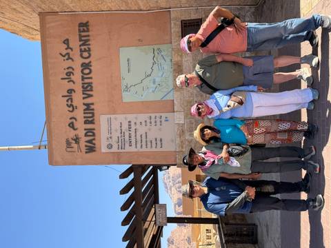 Travelers pose by the signboard at Wadi Rum Visitor Centre under bright desert sun.