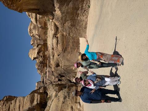 Travelers walk through a rugged sandstone canyon under clear blue skies near Petra.