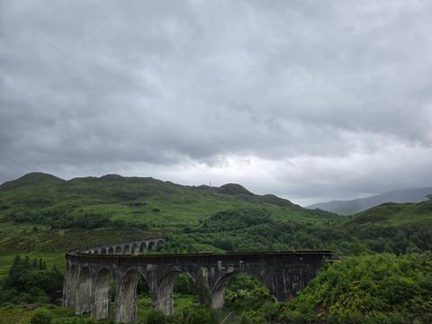 The curving Glenfinnan Viaduct spans a lush green valley beneath thick grey clouds.