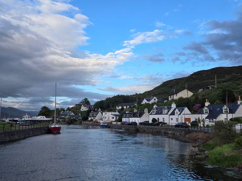 Charming white-washed cottages line a calm inlet with moored boats under a clearing sky.