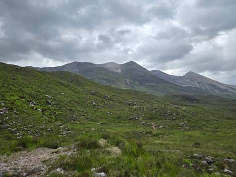 Rolling green moorland leads toward rugged Highland peaks beneath brooding clouds.