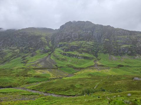 Steep cliff faces draped in emerald vegetation rise above a misty Glencoe valley.