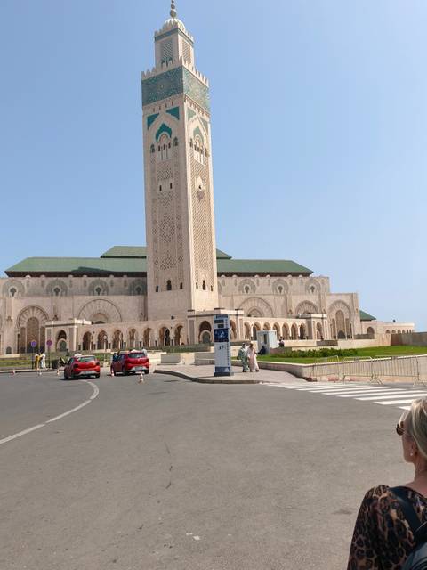 Full facade of Hassan II Mosque captured from street level with cars circling the plaza.