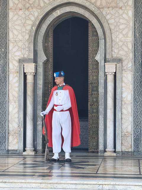 Sentry in white uniform and red cape stands at the ornate marble entrance of the Mausoleum of Mohammed V.