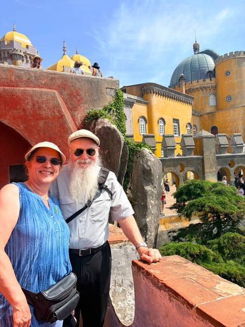Smiling couple pose outside the colourful walls and towers of Pena Palace in Sintra, Portugal.