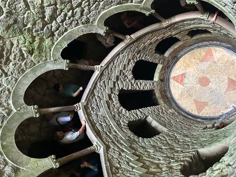 Visitors descend the spiraling Initiation Well at Quinta da Regaleira, framed by moss-covered arches.