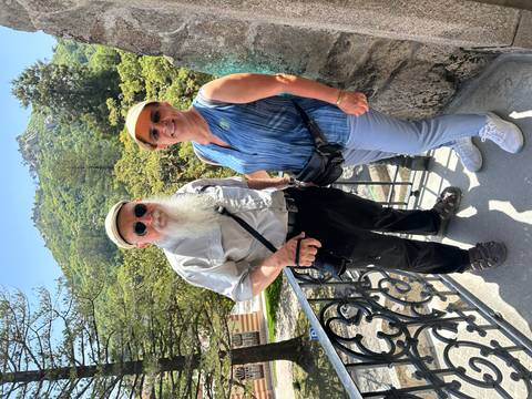 Couple poses on a balcony overlooking wooded hills and castle ruins in Sintra.