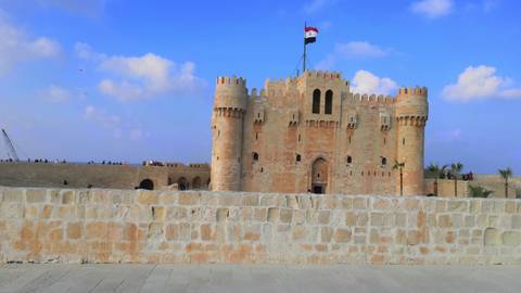 The medieval Citadel of Qaitbay with the Egyptian flag flying against a bright blue sky.