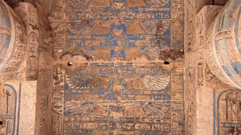Colorful painted ceiling with winged deities and hieroglyphs inside an ancient Egyptian temple.