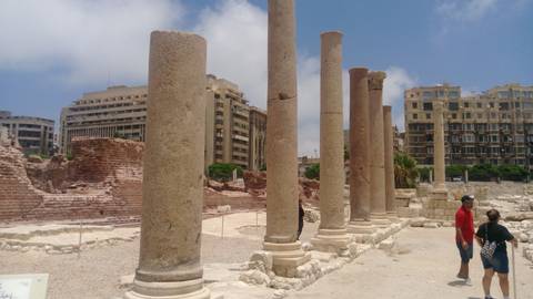 Ruined Roman columns and bricks surrounded by modern Alexandria buildings.