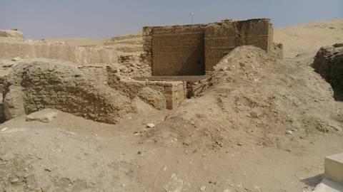 Dusty excavated mud-brick structure in a barren desert setting.