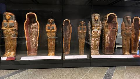 Row of elaborately painted ancient Egyptian coffins on display in a museum case.