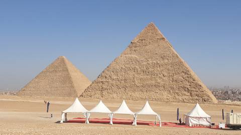 Great Pyramids of Giza rising behind white event tents on the desert plateau.