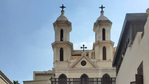 Twin-towered Coptic church façade with crosses rises against a clear blue Cairo sky.