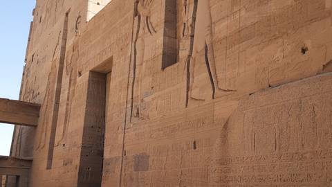 Sandstone walls of ancient Egyptian temple richly carved with large reliefs and hieroglyphs.