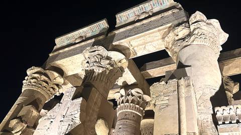 Illuminated stone columns and capitals of Kom Ombo Temple glow against dark night sky.
