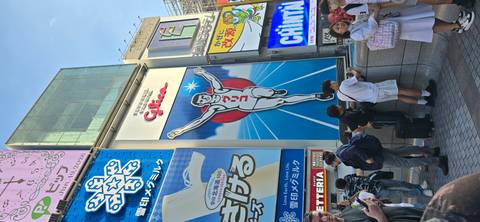 Iconic Glico running man billboard in Dotonbori Osaka surrounded by colorful advertisements and tourists taking photos.