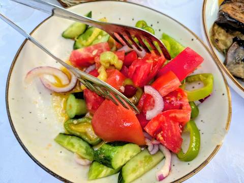 Fresh tomato, cucumber and onion country salad on a rustic plate with serving tongs