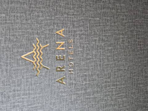 Close-up of a grey textured cover embossed with the gold logo and words 'Arena Hotels'.