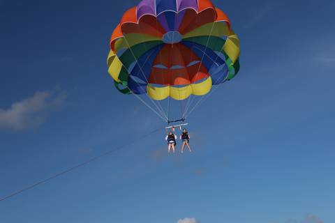 A colorful parasail lifts two thrill-seekers high into a clear blue sky.