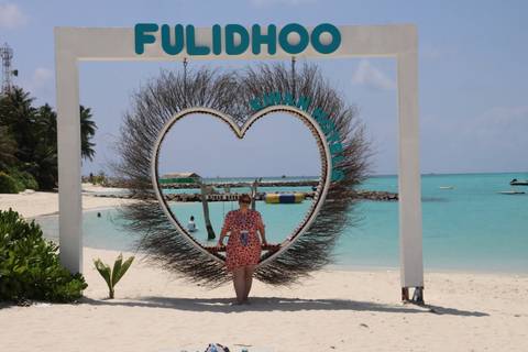 A woman poses inside a giant heart-shaped swing on a pristine white-sand beach with turquoise waters.