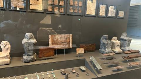Museum showcase with ancient Egyptian statues, tablets and small artifacts behind glass.