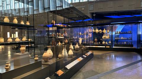 Wide interior shot of museum hall lined with glass cases of ancient pottery under modern lighting.