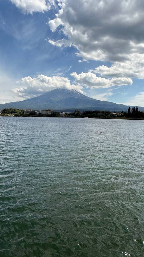 Snow-capped Mount Fuji towers over a calm lake with a town lining the far shore.