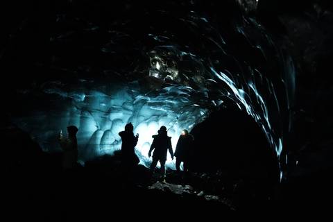 Silhouettes explore a shimmering blue ice cave lit from behind