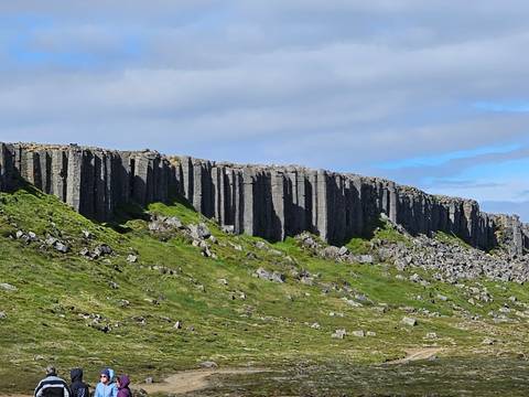 Dramatic wall of gray columnar basalt rising above green grass and scattered rocks
