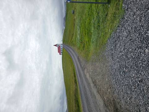Isolated white church with red roof atop a grassy hill under a gray sky, reached by gravel road